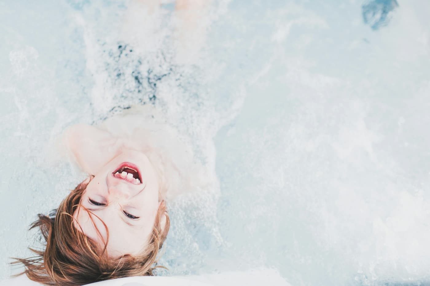 Kind im Wasser, das Gesicht nach oben, lacht und spritzt