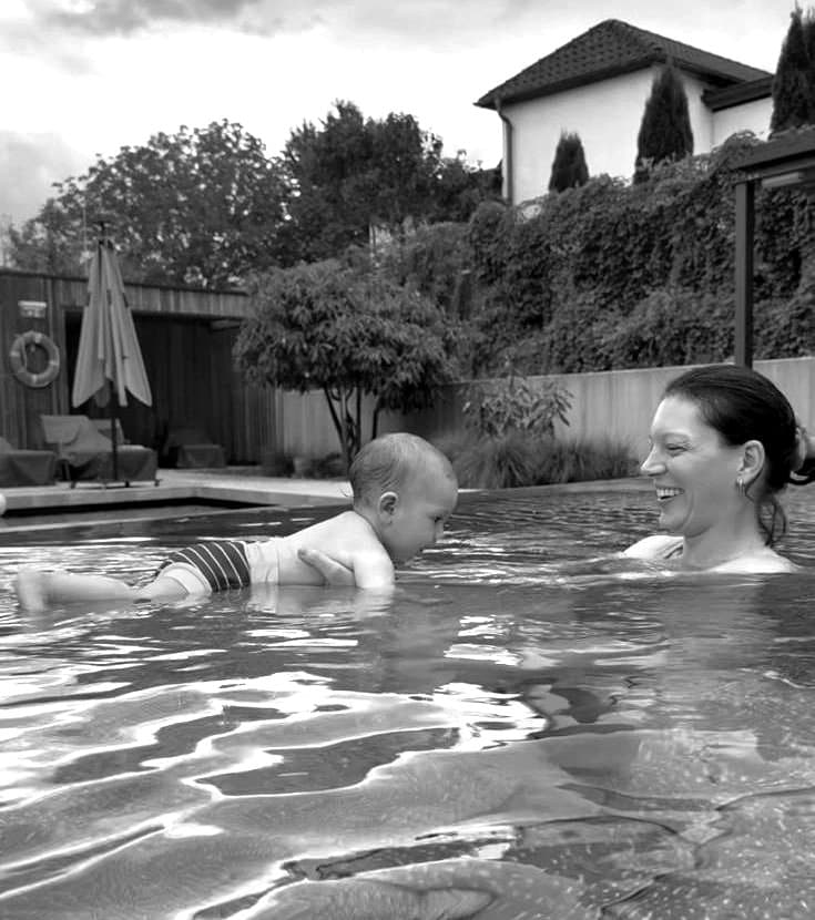Melanie hält ihr Baby im Wasser, das Baby gleitet bäuchlings auf ihren Armen, Schwarzweiß-Aufnahme