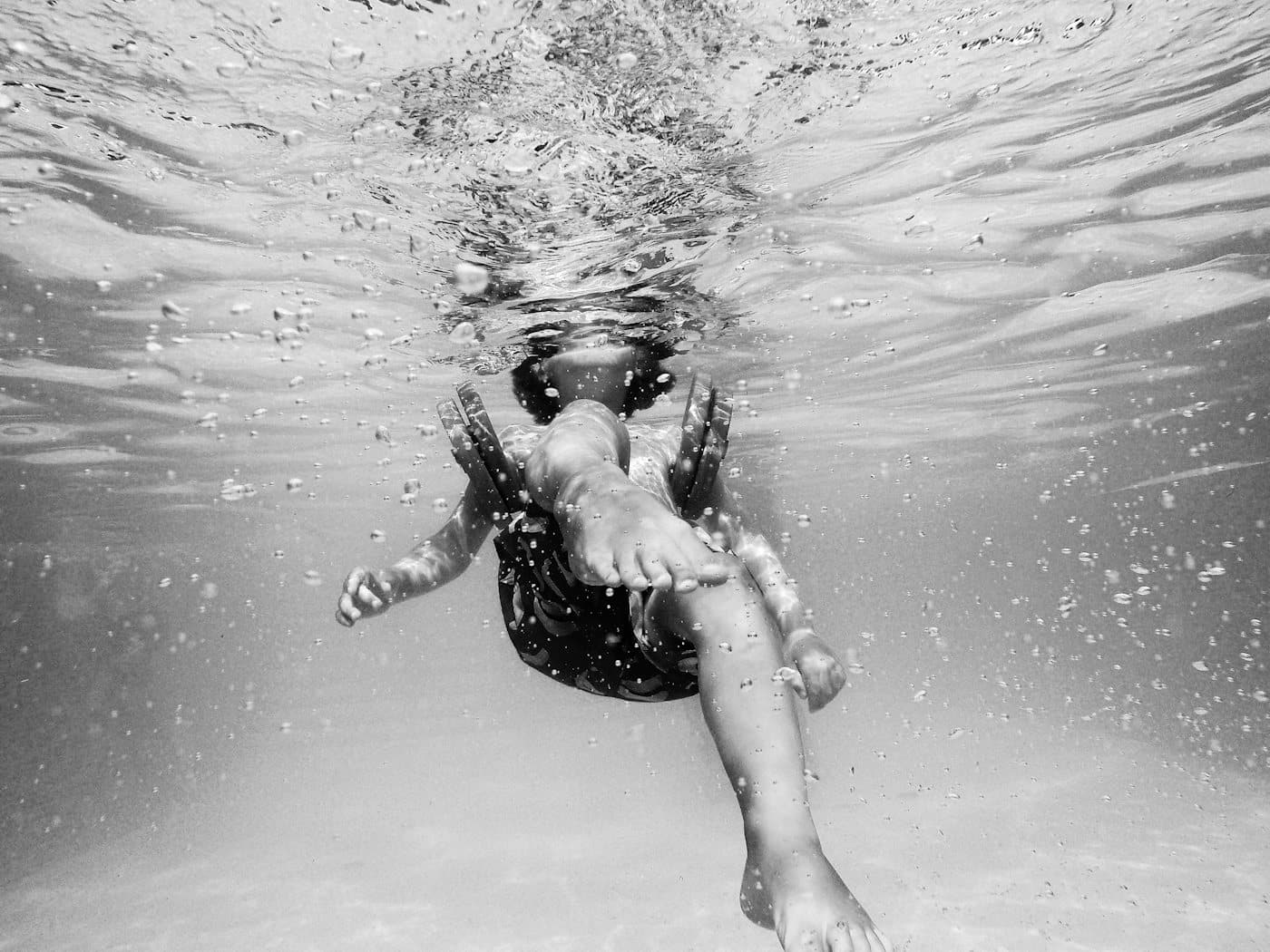 Kind mit Schwimmflügeln im Wasser, Schwarzweiß-Aufnahme von unten