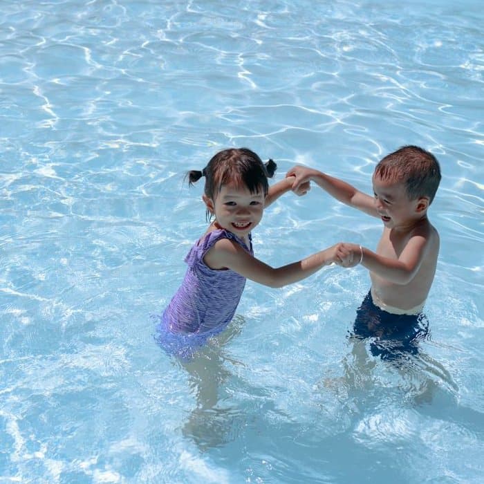 Zwei Kinder halten sich im Wasser an den Händen